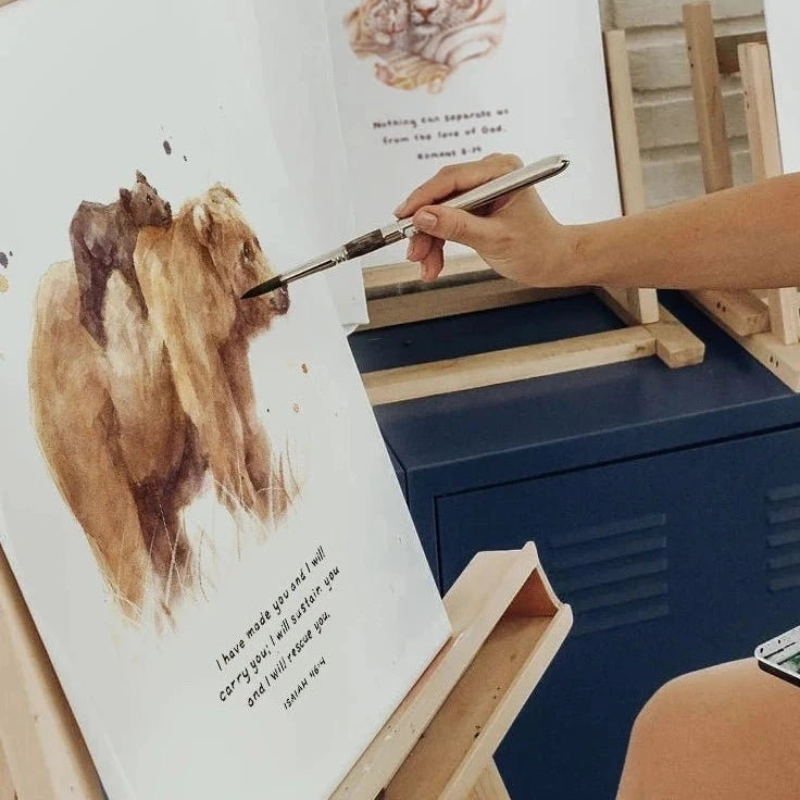 Woman painting bears on an easel with a white brick wall in the background